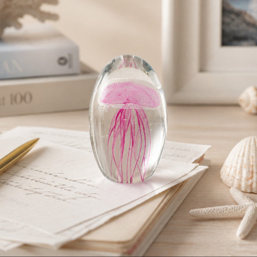 Mellow Monkey pink glass jellyfish paperweight on a desk with seashells and stationery