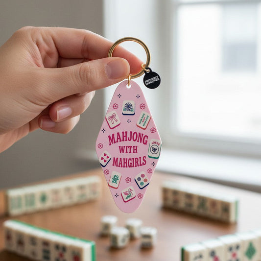 Mellow Monkey pink acrylic motel-style keychain with Mahjong tile illustrations held by a hand over a game table.