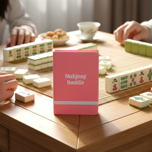 Mellow Monkey pink leatherette pocket journal with Mahjong Baddie embossed on the cover on a mahjong game table.