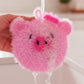 Mellow Monkey pink pig-shaped scrubby sponge with a scrubby texture and a soft side, featuring black eyes and a pink bow.
