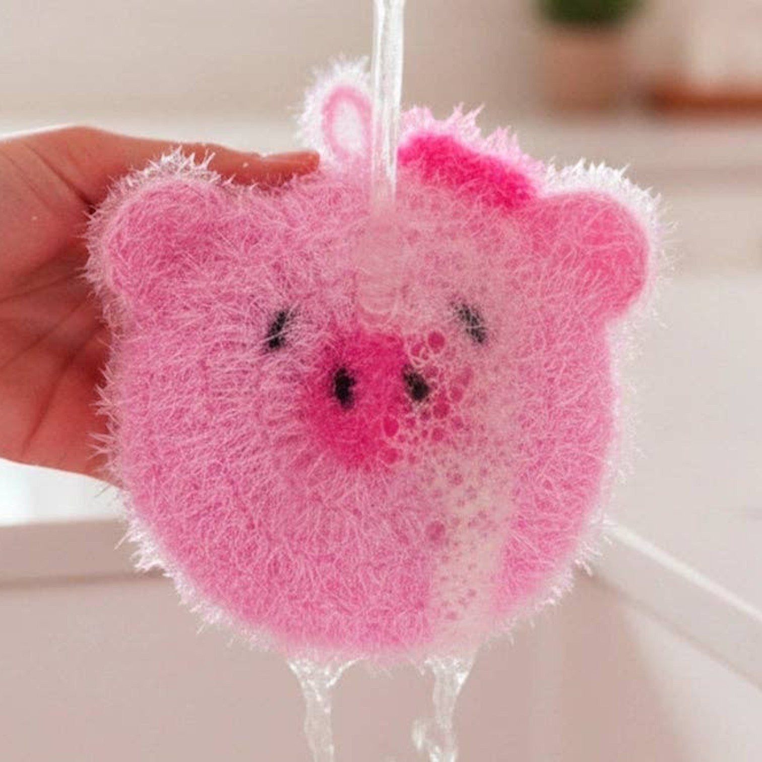 Mellow Monkey pink pig-shaped scrubby sponge with a scrubby texture and a soft side, featuring black eyes and a pink bow.