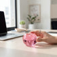 Mellow Monkey pink translucent SlowFlow squishy apple fidget toy on a desk next to a laptop