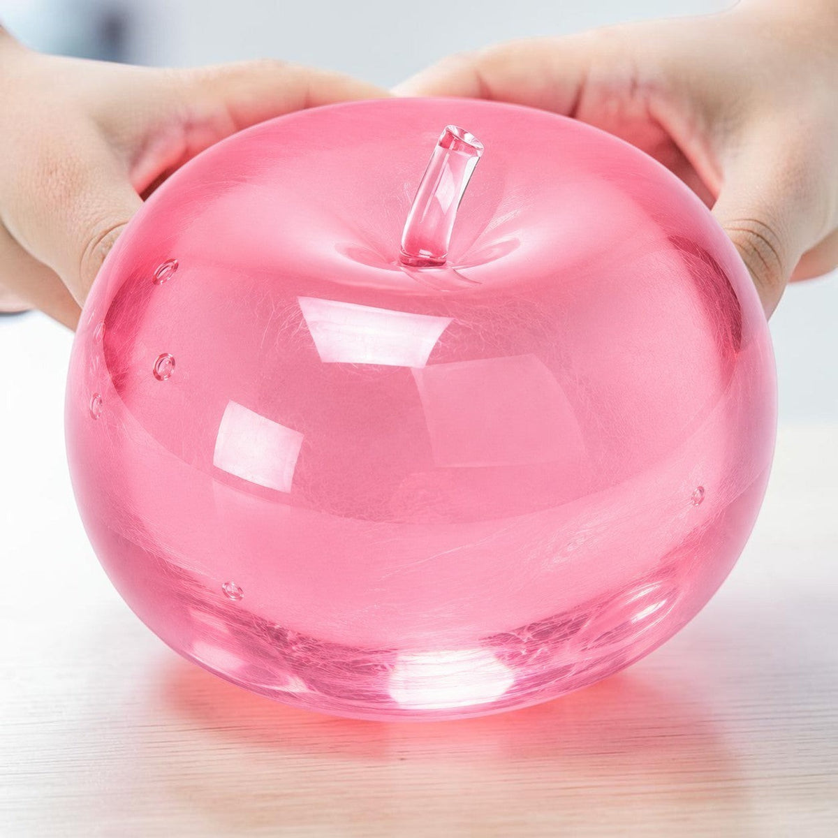 Mellow Monkey Pink Lemonade SlowFlow squishy apple fidget toy being held by two hands on a desk