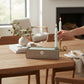 Mellow Monkey pistachio green 7-inch taper candles in a box on a wooden dining table with a hand lighting one candle.