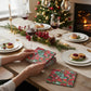 Mellow Monkey Poinsettia cocktail napkins with Kim Hovell artwork held over a festive holiday dinner table setting.