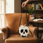 Mellow Monkey glow in the dark poisoned apple crossbody bag in white and black vinyl held over a leather armchair.