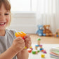 A child smiling while squeezing a glittery Mellow Monkey popsicle-shaped stress toy in a bright playroom.