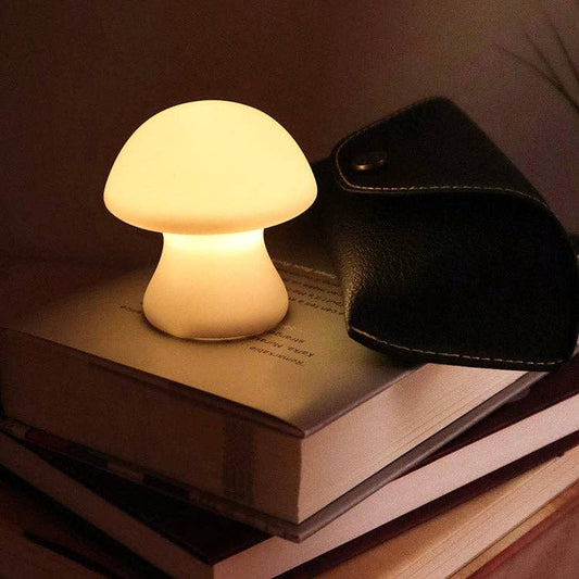 Mellow Monkey small mushroom-shaped porcelain LED lamp emitting a warm, diffuse glow on a stack of books.