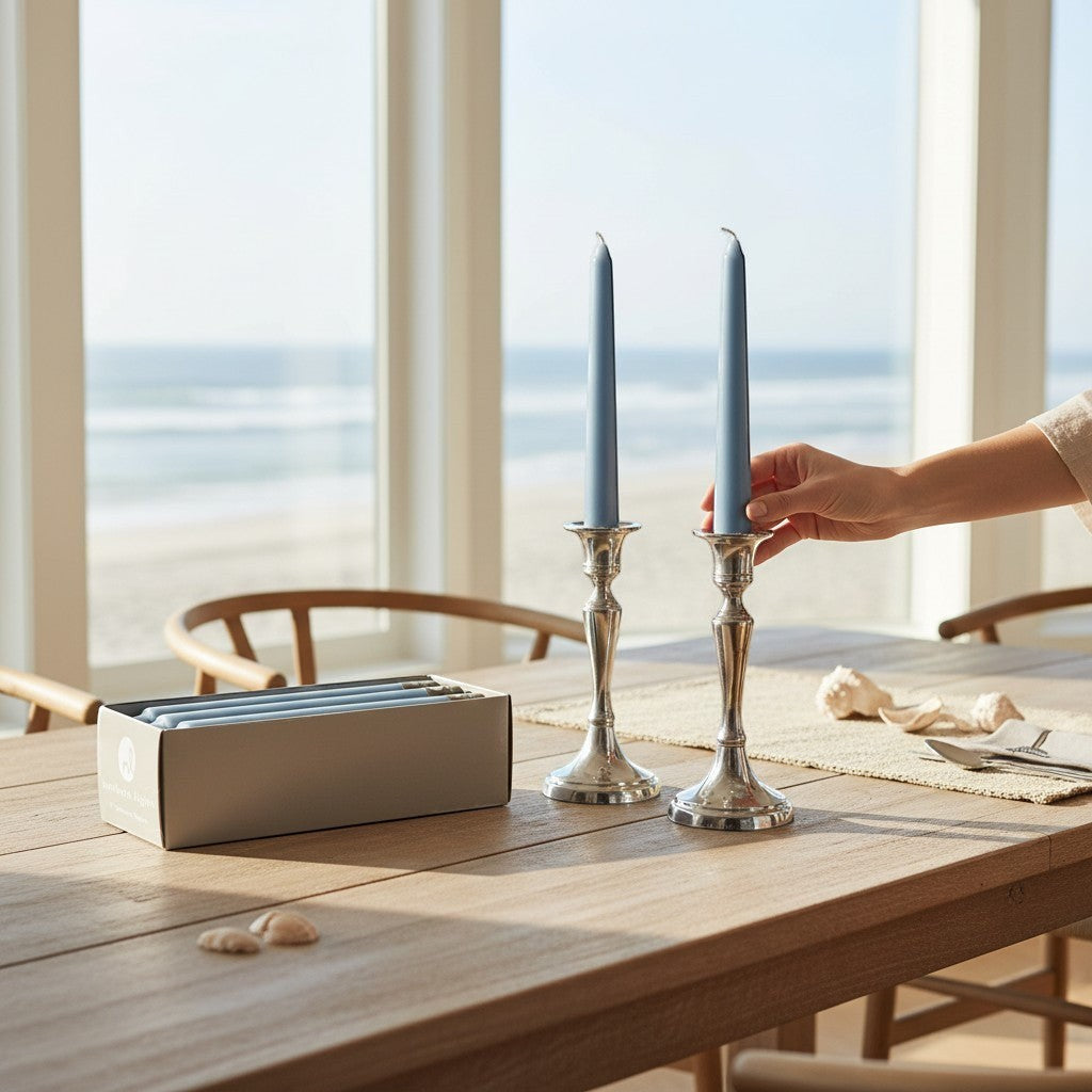 Mellow Monkey prairie blue 7-inch taper candles in silver holders on a wooden table by the beach.