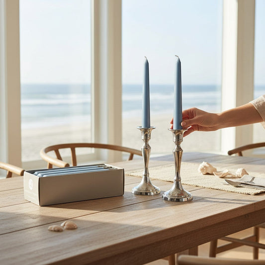 Mellow Monkey prairie blue 7-inch taper candles in silver holders on a wooden table by the beach.