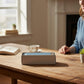 Mellow Monkey 7-inch prairie blue taper candles in a 12-piece box set on a wooden table in a sunlit room.