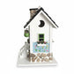 Mellow Monkey Primrose Cottage birdhouse with white exterior, black roof, stone chimney, and hand-painted floral motif.