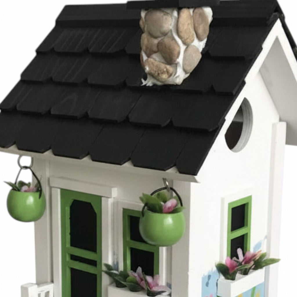 Mellow Monkey Primrose Cottage birdhouse with white exterior, black roof, green door and windows, and floral motif with river rocks.