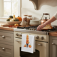 Mellow Monkey white cotton flour sack towel featuring a watercolor pumpkin stack print hanging on a kitchen oven