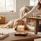 Mellow Monkey Pumpkin Spice Pet House candle in a glass jar on a wooden table with a golden retriever in the background