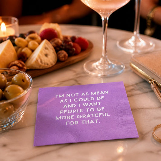 Mellow Monkey purple cocktail napkin with white text reading I'm not as mean as I could be on a marble table