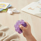 Mellow Monkey Purple Haze Feelzies sensory bracelet being squeezed by a child's hand, featuring glittery purple gel.