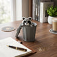 Mellow Monkey articulated grey and white raccoon fidget toy sitting inside a matching grey plastic trash can on a desk