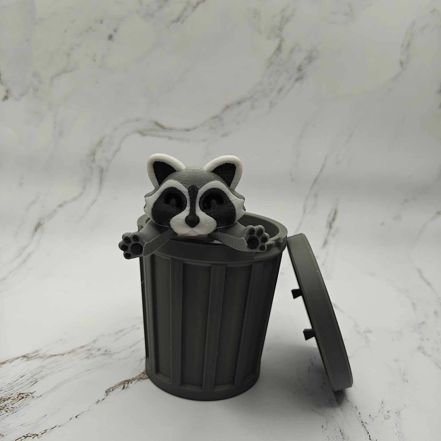 Mellow Monkey articulated raccoon fidget toy in a grey 3D printed trash can on a marble surface