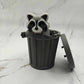 Mellow Monkey articulated raccoon fidget toy emerging from a grey 3D printed plastic trash can on a marble surface.