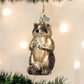 Mellow Monkey Raccoon glass ornament with black mask and bushy tail, hanging on a Christmas tree.