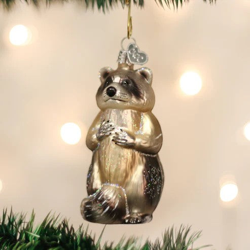 Mellow Monkey Raccoon glass ornament with black mask and bushy tail, hanging on a Christmas tree.