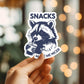 Mellow Monkey vinyl sticker featuring a cute raccoon drinking from a cup with the text Snacks Make Me Nicer