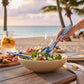 Mellow Monkey Race Day melamine salad utensils with blue and white abstract art, serving a salad on a beach.