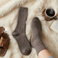 Mellow Monkey Ragg Stone crew socks with ribbed texture worn on a cozy faux fur rug next to a steaming coffee mug.