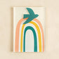 Mellow Monkey Together Tile acrylic wall art with a teal bird flying over a rainbow in peach, yellow, and teal.