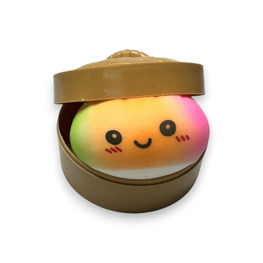 Mellow Monkey tie-dye rainbow dumpling sensory squeeze toy with a cute smiling face inside a brown steamer basket.