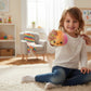 Mellow Monkey tie-dye rainbow dumpling squeeze toy with a cute face held by a smiling child in a bright playroom.