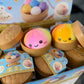 Mellow Monkey tie-dye rainbow dumpling sensory squeeze toy with a cute face in a miniature bamboo steamer container.