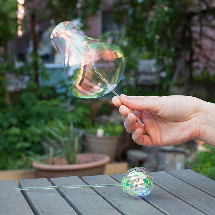 Mellow Monkey rainbow spinner toy creating iridescent bubble-like shapes in an outdoor garden setting.
