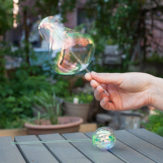 Mellow Monkey rainbow spinner toy creating iridescent bubble-like shapes in an outdoor garden setting.