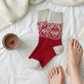 Mellow Monkey Red Confetti holiday crew socks with snowflake pattern on white bedding next to hot cocoa and a book.