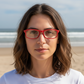 Mellow Monkey Spare Pair reading glasses with vibrant red frames worn by a woman on a sunny beach.