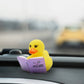 Mellow Monkey yellow rubber duck reading a purple book titled I Like My Books Extra Spicy on a car dashboard
