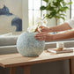 Mellow Monkey round capiz shell vase in blue and white with iridescent texture, styled on a wooden console table.