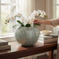 Mellow Monkey round capiz shell vase in soft green with white orchid flowers on a wooden console table