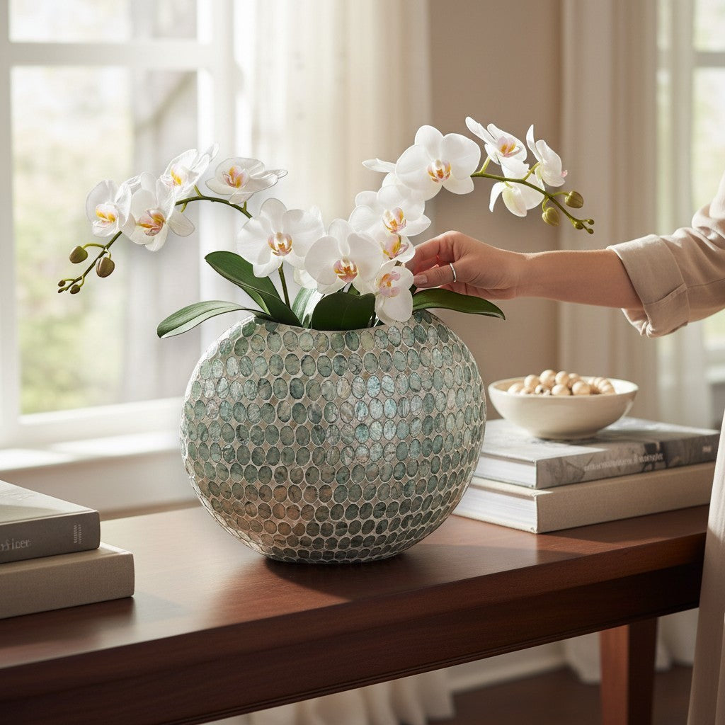 Mellow Monkey round capiz shell vase in soft green with white orchid flowers on a wooden console table