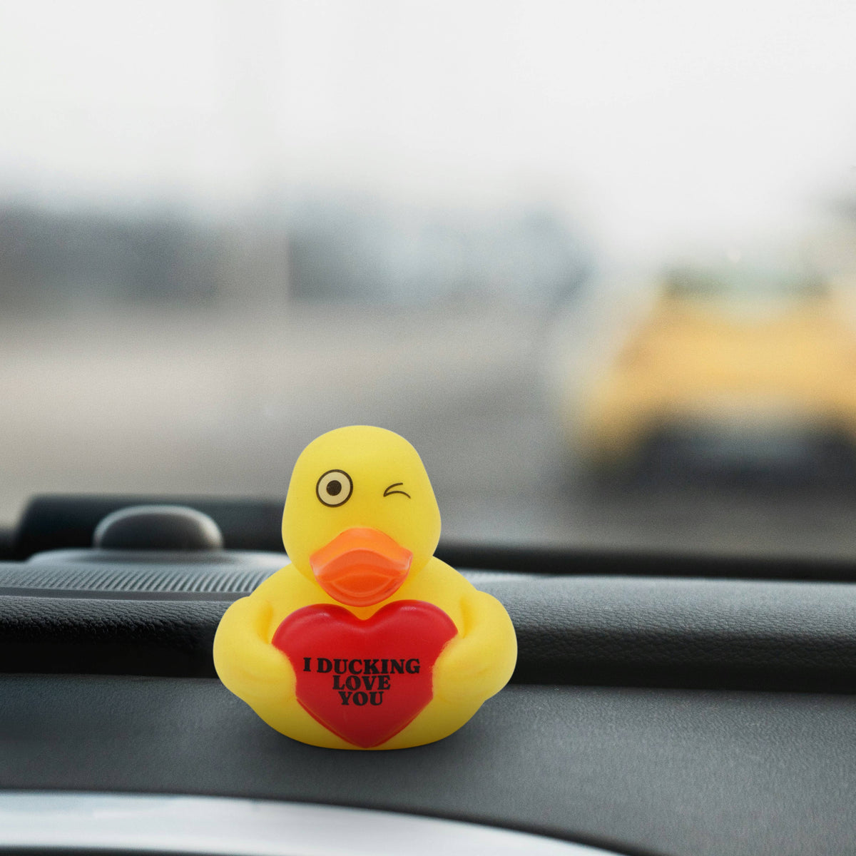 Mellow Monkey yellow rubber duck with a winking eye holding a red heart that says I Ducking Love You on a dashboard