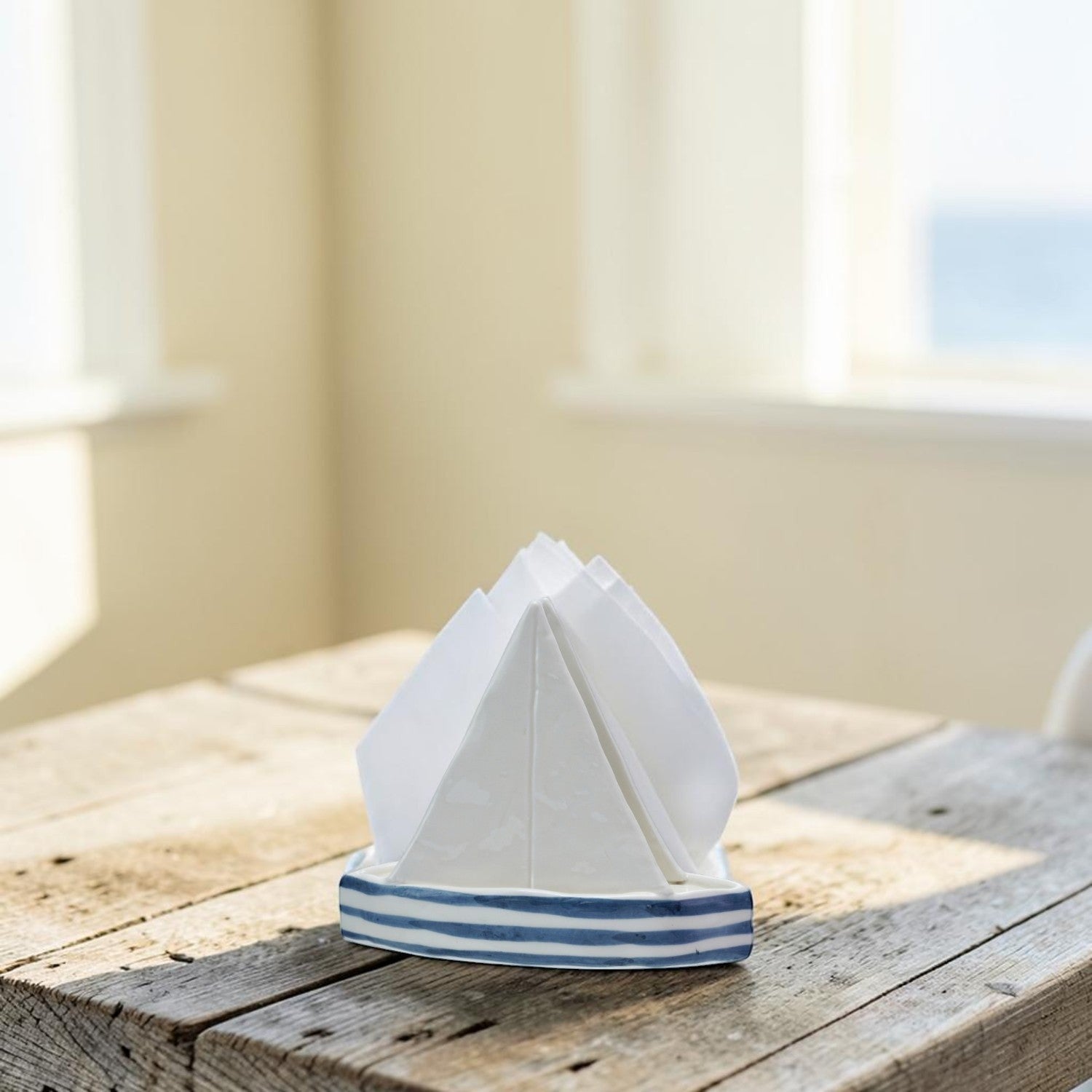 Mellow Monkey stoneware sailboat napkin holder with blue and white stripes on a rustic wooden table