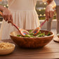 Mellow Monkey Marrakesh Collection salad serving utensil set, made of layered birch with vibrant colors, used by a woman tossing salad at a rooftop party.