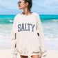 Woman wearing a Mellow Monkey sand-colored crewneck sweatshirt with a distressed blue SALTY graphic at the beach.