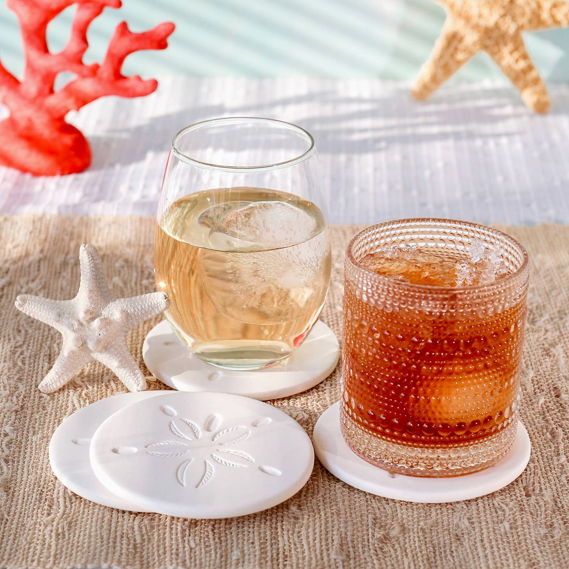 Mellow Monkey set of four white sandstone coasters with sand dollar designs on a beach-themed table setting.