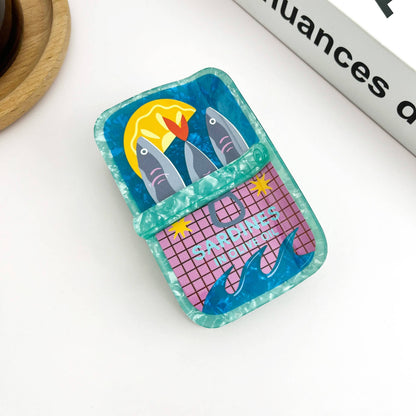 Mellow Monkey sardine can hair claw clip in blue and pink acrylic with a quirky fish and lemon graphic design.
