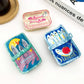 Mellow Monkey sardine can hair claw clips in three colorful, quirky designs with fish and tomato illustrations.