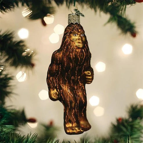 Mellow Monkey Sasquatch blown glass holiday ornament, brown with glitter accents, hanging on a Christmas tree.