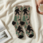 Mellow Monkey Sasquatch sleeper crew socks in plush beige, black, and green forest pattern on a soft white blanket.